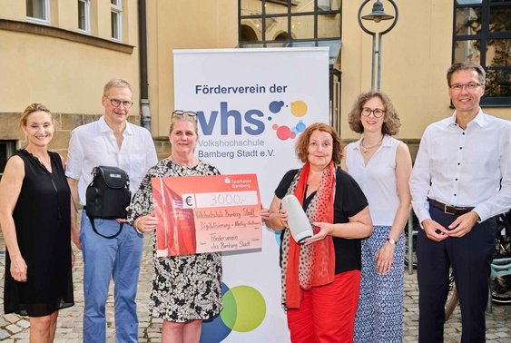 Fünf Personen aus dem Vorstand des VHS-Fördervereins übergeben einen Spendenscheck und eine Meeting-Owl für Hybridkurse an VHS-Leiterin Dr. Anna Scherbaum