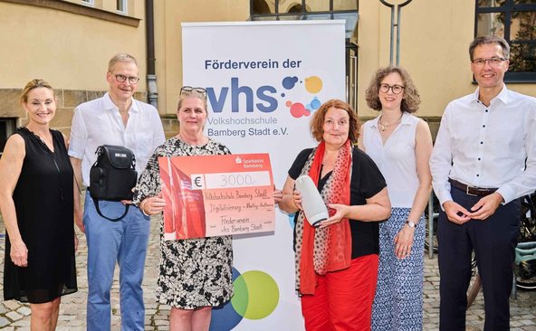 Fünf Personen aus dem Vorstand des VHS-Fördervereins übergeben einen Spendenscheck und eine Meeting-Owl für Hybridkurse an VHS-Leiterin Dr. Anna Scherbaum