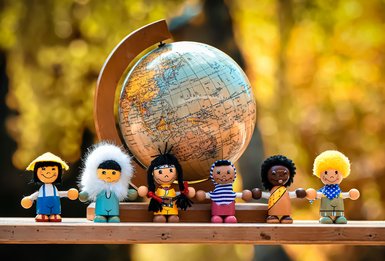 6 Kinderfiguren aus unterschiedlichen Ländern vor einem Globus