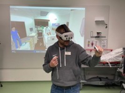 Ein Mann hat eine VR-Brille auf und "übt" Pflegehandgriffe