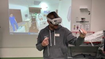 Ein Mann hat eine VR-Brille auf und "übt" Pflegehandgriffe