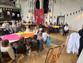 Das Bild zeigt die Gäste, die an geschmückten Tischen im farbenfroh dekorierten Großen Saal sitzen.