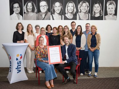 vhs-Leitung Dr. Anna Scherbaum und Oberbürgermeister Sebastian M. Niedermaier halten die Urkunde des 3-Sterne-Assessments in den Händen. Dahinter das vhs-Team