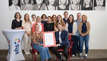vhs-Leitung Dr. Anna Scherbaum und Oberbürgermeister Sebastian M. Niedermaier halten die Urkunde des 3-Sterne-Assessments in den Händen. Dahinter das vhs-Team