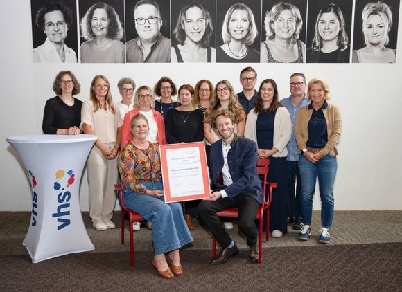 Foto: Stadtarchiv Bamberg, Nadine Gumpert vhs-Leitung Dr. Anna Scherbaum und Oberbürgermeister Sebastian M. Niedermaier halten die Urkunde des 3-Sterne-Assessments in den Händen. Dahinter das vhs-Team